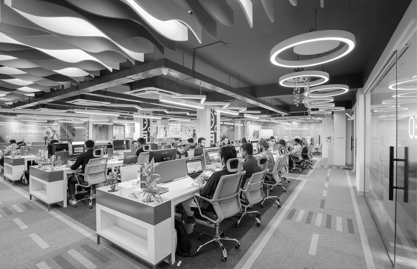 Spacious open-plan office with rows of desks and striking circular ceiling lights.