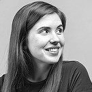 Portrait of a woman with straight long hair, in a dark t-shirt, set against a neutral backdrop.